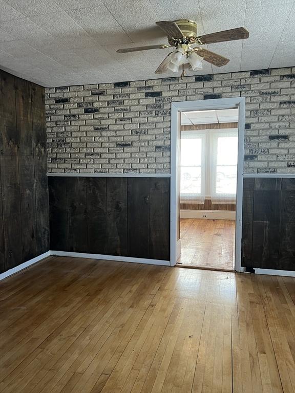 unfurnished room featuring a ceiling fan, baseboards, wooden walls, and hardwood / wood-style floors