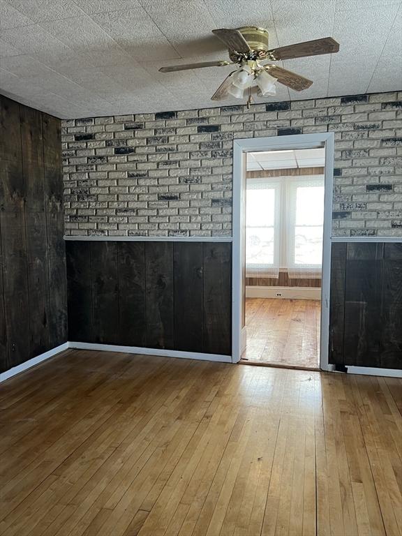 spare room featuring a ceiling fan, wood-type flooring, wooden walls, and baseboards