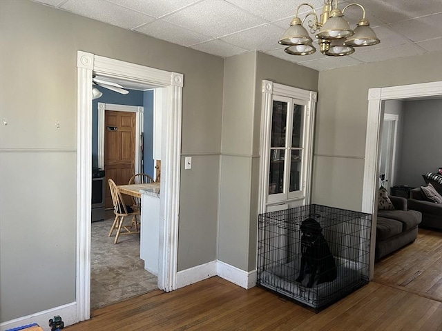 hallway featuring baseboards, a drop ceiling, hardwood / wood-style flooring, and a notable chandelier