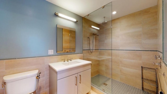 bathroom featuring vanity, a tile shower, tile walls, and toilet