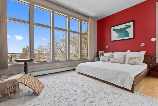 bedroom with a baseboard radiator, an accent wall, wood finished floors, and multiple windows