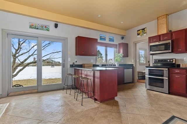 kitchen featuring stainless steel appliances, a peninsula, a sink, dark brown cabinets, and dark countertops