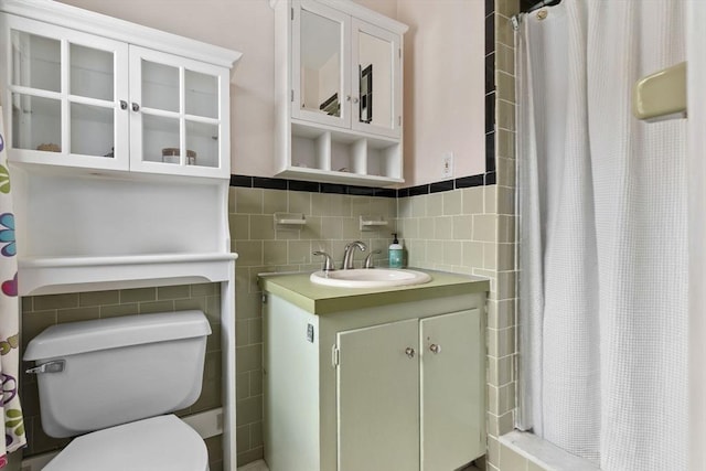 full bathroom with wainscoting, toilet, a tile shower, vanity, and tile walls