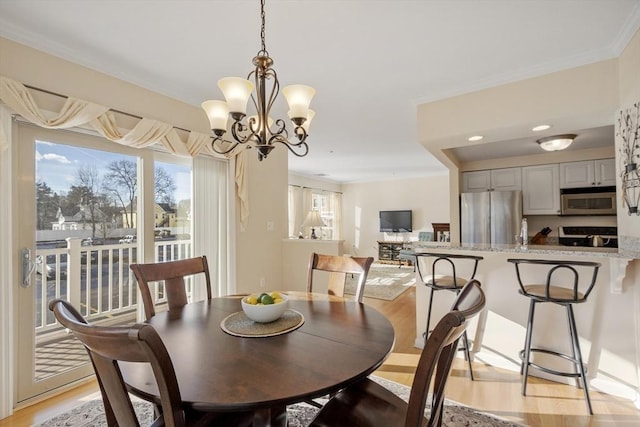 dining space with an inviting chandelier, ornamental molding, and light wood-type flooring