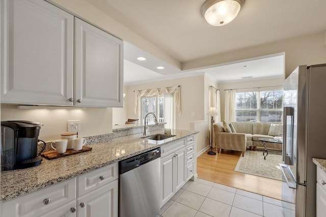 kitchen featuring a wealth of natural light, sink, white cabinets, stainless steel appliances, and light stone countertops