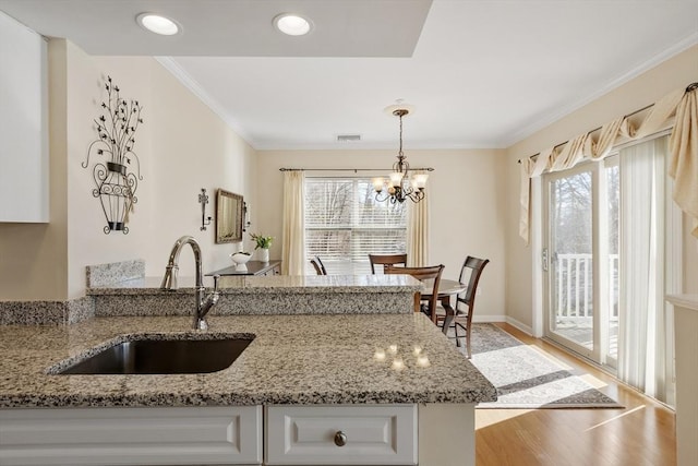 kitchen featuring white cabinetry, ornamental molding, light stone countertops, and sink