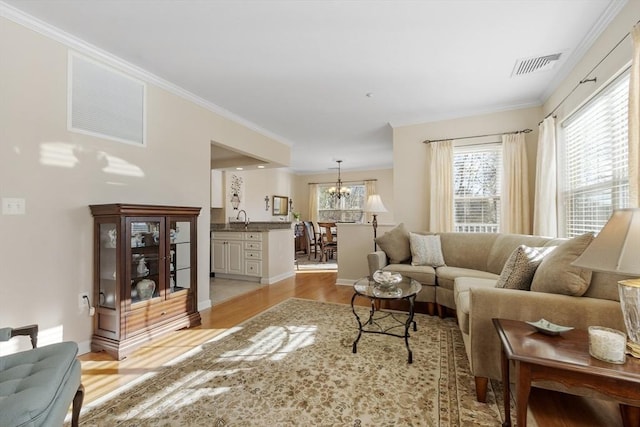 living room featuring ornamental molding, sink, a notable chandelier, and light hardwood / wood-style flooring