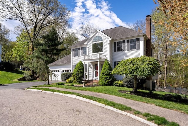 view of front of house with a balcony, a front yard, a chimney, an attached garage, and driveway