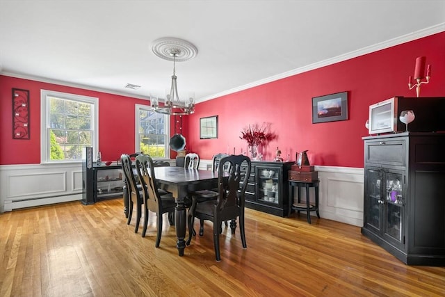 dining area featuring ornamental molding, wainscoting, wood finished floors, a baseboard heating unit, and a notable chandelier