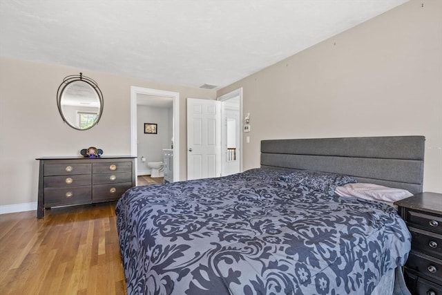 bedroom with baseboards, wood finished floors, and connected bathroom