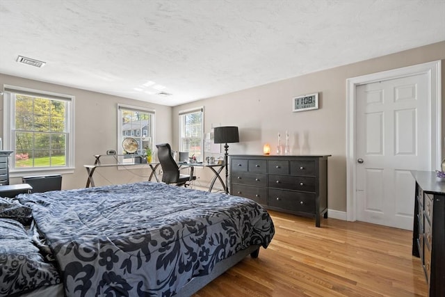 bedroom featuring a textured ceiling, baseboards, visible vents, and wood finished floors