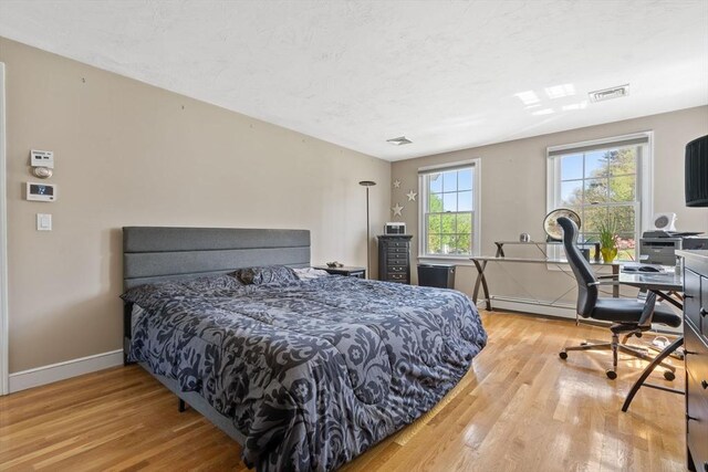 bedroom featuring visible vents, baseboards, light wood finished floors, and a baseboard heating unit