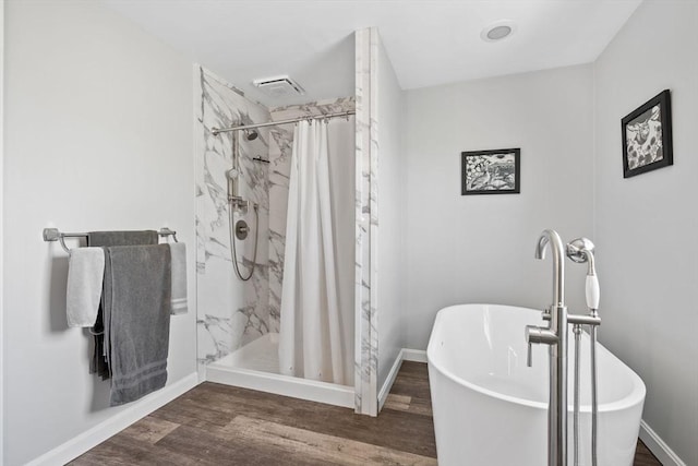 full bath with a freestanding bath, a marble finish shower, baseboards, and wood finished floors