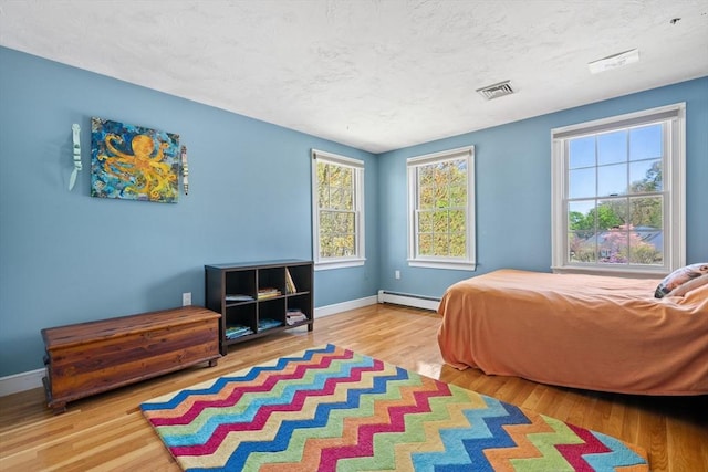 bedroom featuring a baseboard heating unit, baseboards, visible vents, and wood finished floors
