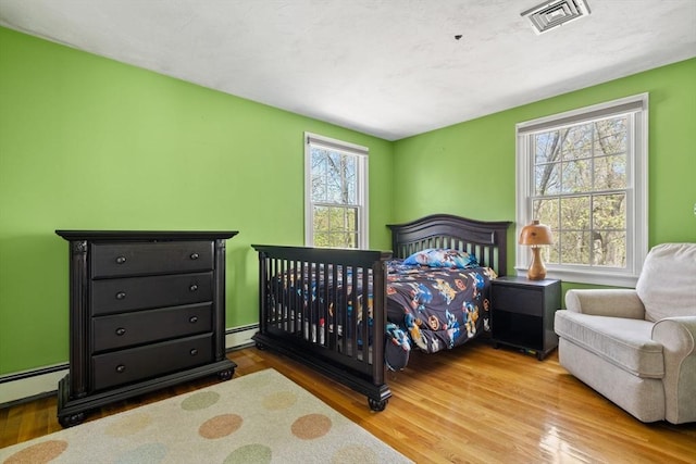 bedroom featuring baseboard heating, visible vents, wood finished floors, and a baseboard radiator