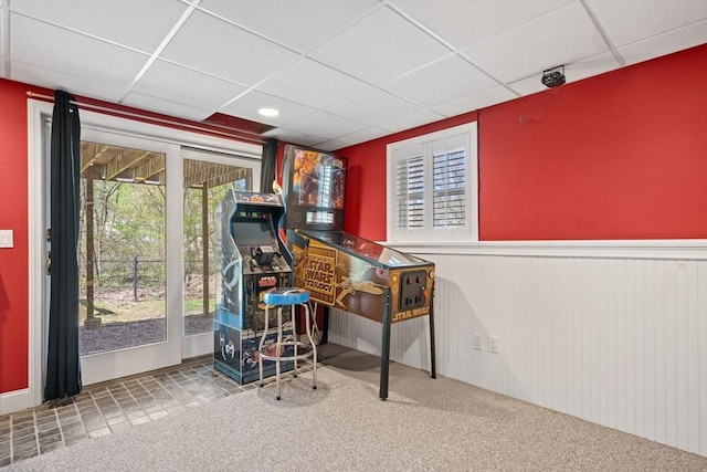 recreation room with carpet floors, a wealth of natural light, a paneled ceiling, and a wainscoted wall