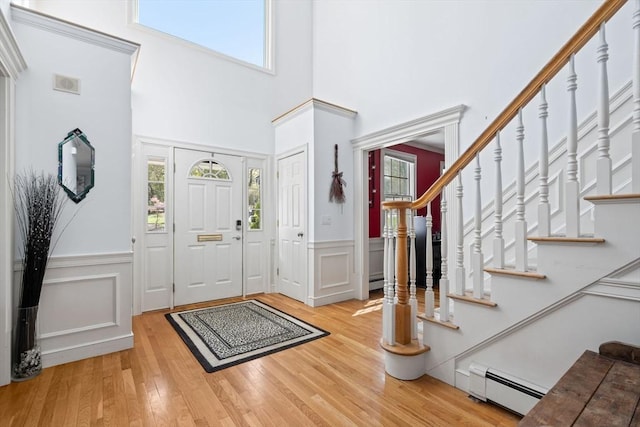 foyer entrance featuring a wainscoted wall, stairs, wood finished floors, a towering ceiling, and a baseboard heating unit