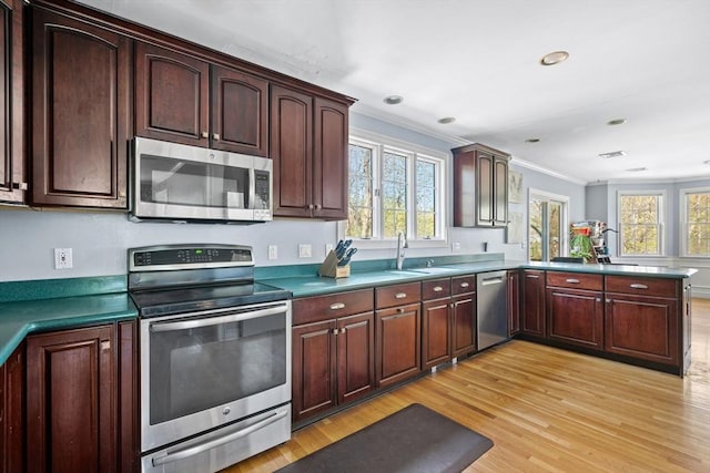 kitchen featuring crown molding, a sink, a peninsula, light wood-style floors, and stainless steel appliances