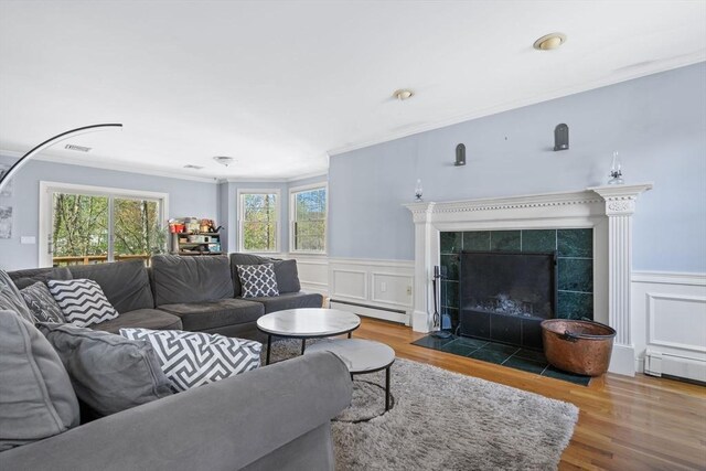 living area featuring wainscoting, ornamental molding, baseboard heating, and wood finished floors