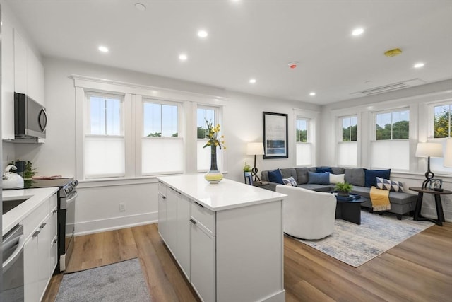 kitchen with white cabinets, a kitchen island, wood-type flooring, and appliances with stainless steel finishes