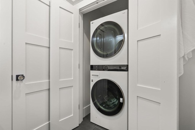 clothes washing area featuring dark tile patterned floors and stacked washer / drying machine