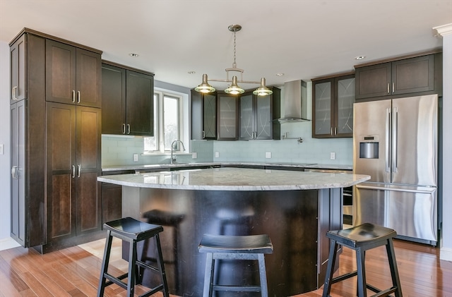 kitchen featuring wood-type flooring, wall chimney range hood, a center island, dark brown cabinetry, and stainless steel fridge with ice dispenser