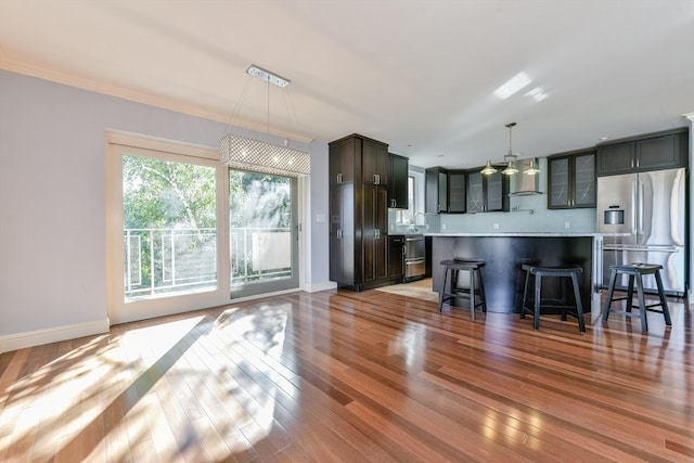 kitchen featuring light wood-type flooring, a center island, a kitchen breakfast bar, wall chimney exhaust hood, and stainless steel refrigerator with ice dispenser