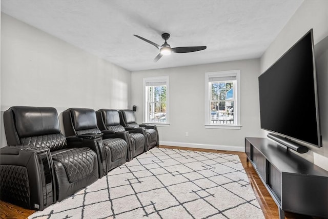 home theater room featuring ceiling fan, wood finished floors, and baseboards