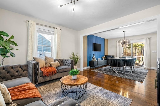 living room featuring baseboards, wood finished floors, a wealth of natural light, and an inviting chandelier