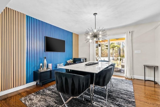 dining space with an inviting chandelier, an accent wall, wood finished floors, baseboards, and wallpapered walls