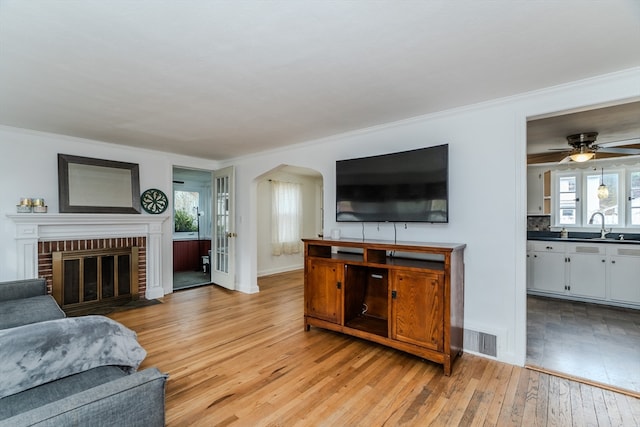 living room featuring sink, ceiling fan, light wood-type flooring, a fireplace, and ornamental molding