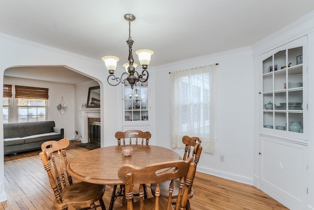 dining space with a notable chandelier, light hardwood / wood-style floors, crown molding, and a fireplace