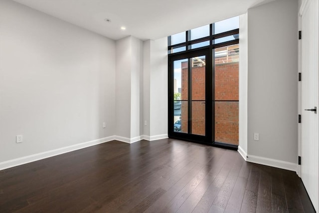 spare room featuring dark wood-style floors, baseboards, a wall of windows, and recessed lighting