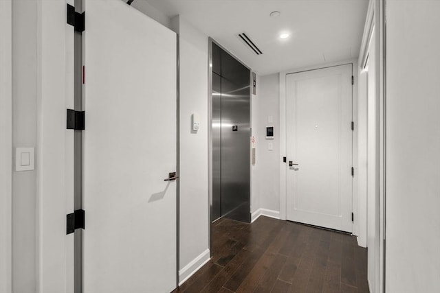 hallway with dark wood-style floors, elevator, visible vents, and baseboards