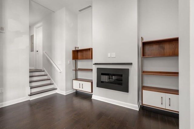 unfurnished living room featuring visible vents, dark wood finished floors, baseboards, electric panel, and a glass covered fireplace