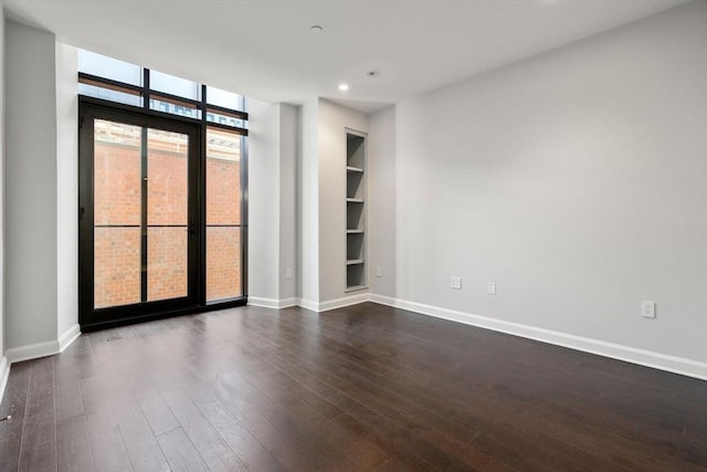 empty room featuring dark wood-style floors, built in shelves, baseboards, and floor to ceiling windows