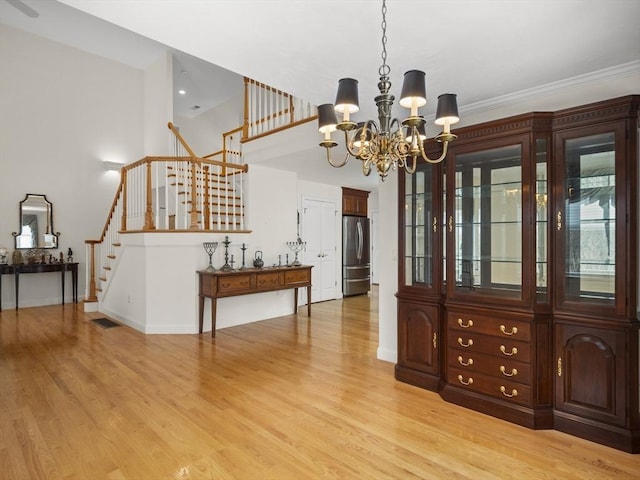 dining space featuring visible vents, a chandelier, light wood-type flooring, baseboards, and stairs