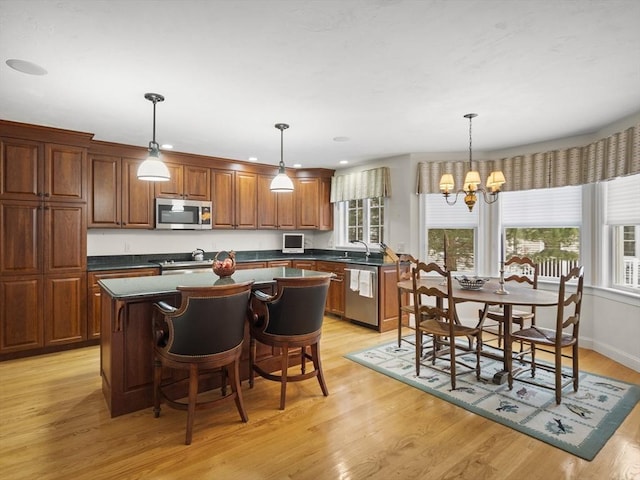 kitchen with light wood finished floors, dark countertops, appliances with stainless steel finishes, a center island, and an inviting chandelier