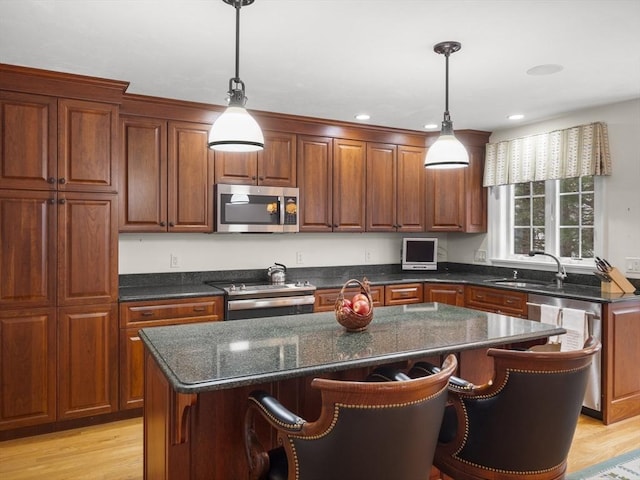 kitchen featuring appliances with stainless steel finishes, a kitchen island, a sink, and light wood-style flooring