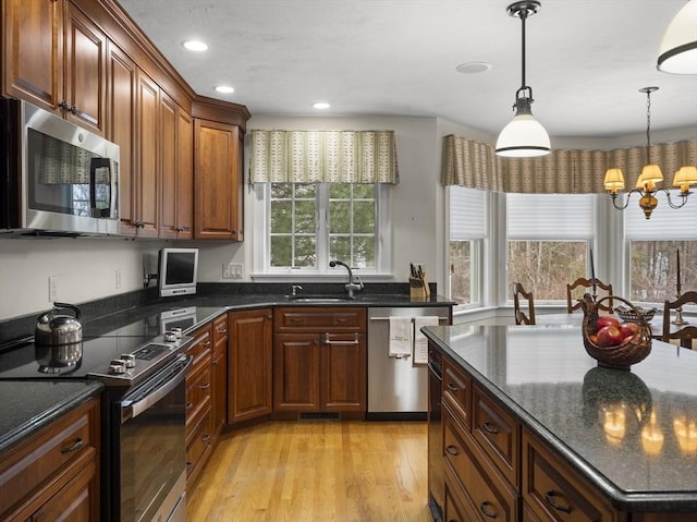 kitchen featuring dark stone countertops, hanging light fixtures, stainless steel appliances, light wood-style floors, and a sink