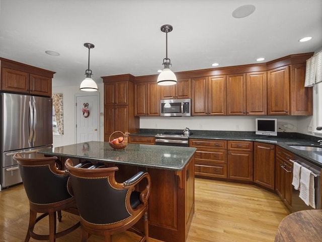 kitchen with light wood-type flooring, appliances with stainless steel finishes, hanging light fixtures, and a center island