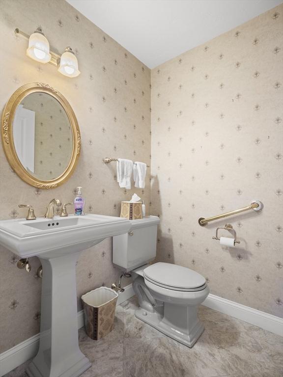 half bath with baseboards, a sink, toilet, and wallpapered walls