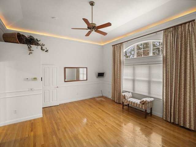 unfurnished room featuring light wood-type flooring, a tray ceiling, and baseboards