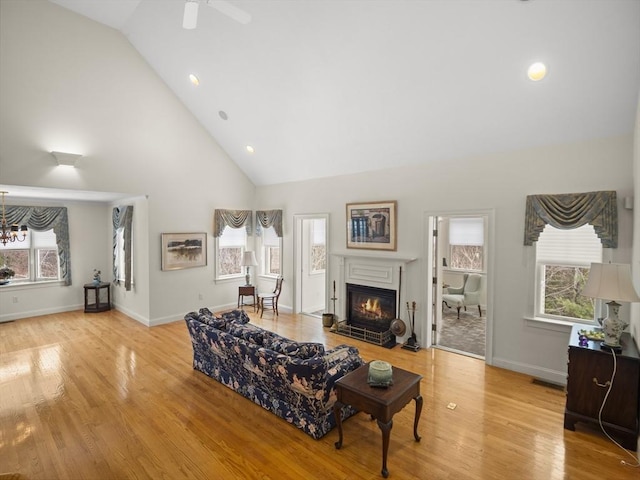 living area featuring high vaulted ceiling, a glass covered fireplace, baseboards, and light wood finished floors