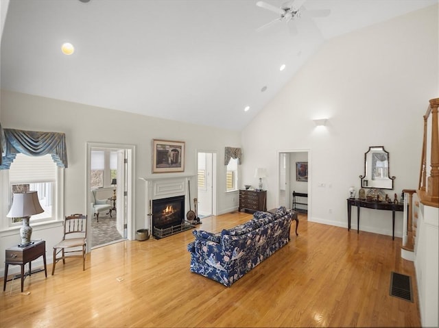 living area featuring high vaulted ceiling, a fireplace with flush hearth, visible vents, and light wood-style floors