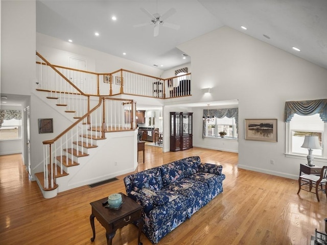 living area featuring high vaulted ceiling, stairs, baseboards, and wood finished floors