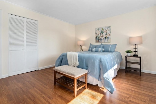 bedroom with wood finished floors, baseboards, a closet, and crown molding