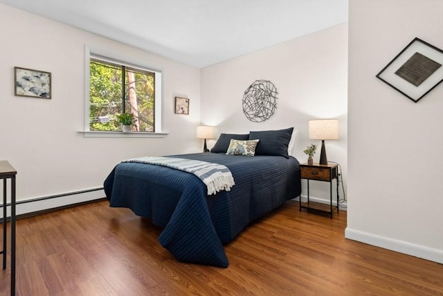 bedroom featuring wood finished floors, a baseboard heating unit, and baseboards