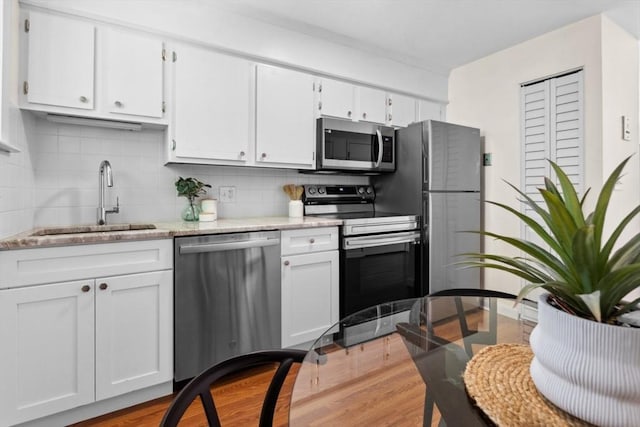 kitchen featuring appliances with stainless steel finishes, a sink, decorative backsplash, and white cabinets