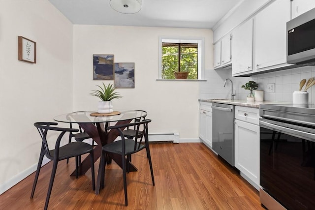 kitchen featuring stainless steel appliances, backsplash, white cabinets, a sink, and light wood-style floors